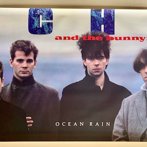 May include: A vintage concert poster for Echo & the Bunnymen, featuring a photo of the band members in front of a cloudy sky. The poster is blue, white, and red with the band's name and the album title "Ocean Rain" printed on it.