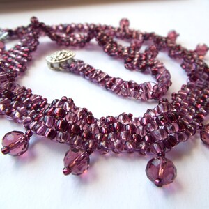 May include: A purple beaded necklace with a layered design and dangling crystal beads.