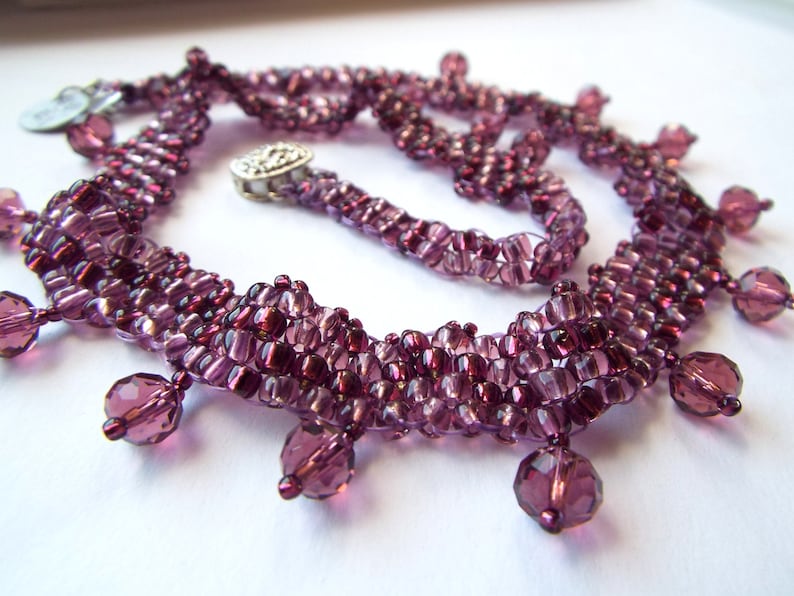 May include: A purple beaded necklace with a layered design and dangling crystal beads.