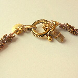 May include: A gold-toned necklace with a toggle clasp and a brown and gold beaded chain. A small, gray gemstone dangles from the clasp.