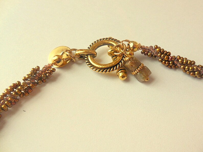 May include: A gold-toned necklace with a toggle clasp and a brown and gold beaded chain. A small, gray gemstone dangles from the clasp.