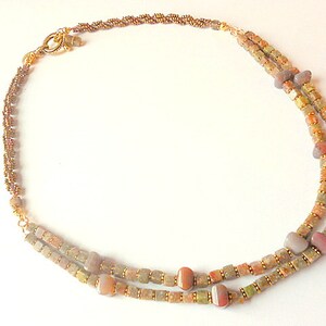 May include: A double-strand necklace with brown, gold, and white beads. The necklace has a gold clasp and is made of natural materials.