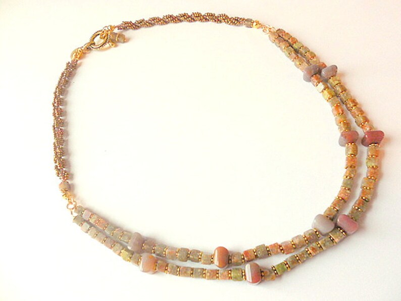 May include: A double-strand necklace with brown, gold, and white beads. The necklace has a gold clasp and is made of natural materials.