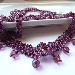 May include: A purple beaded necklace with a fringe of dangling beads. The necklace is made of small, faceted beads that are strung together in a delicate pattern.