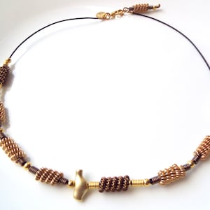 Pode incluir: Um colar de fio dourado e marrom com um pingente de pássaro. O colar é feito de pequenas contas de fio enroladas e tem um design simples e elegante.
