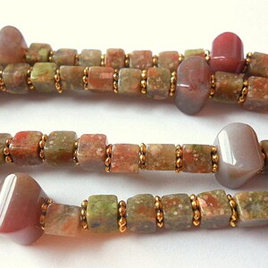 May include: A multi-strand necklace made with brown, green, and pink gemstone beads. The beads are separated by small gold beads.