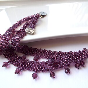 May include: A multi-strand necklace with a silver charm and purple glass beads. The necklace has a fringe of purple beads.