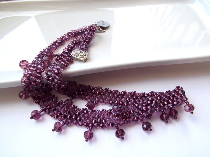 May include: A multi-strand necklace with a silver charm and purple glass beads. The necklace has a fringe of purple beads.