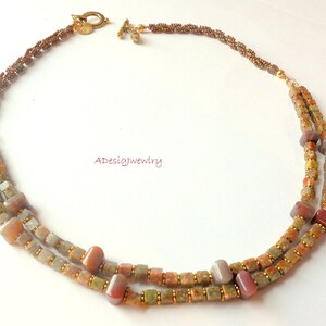 May include: A double-strand necklace with brown, green, and red square beads. The necklace is made with a gold-tone chain and clasp.