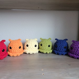 May include: A row of seven crocheted octopus plushies in rainbow colors, from red to purple, with black eyes.