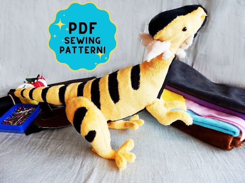 May include: A plush toy lizard in yellow and black stripes, with a black head and tail. The toy has white accents and is lying on a surface. A teal circle with the text "PDF SEWING PATTERN!" is in the upper left.