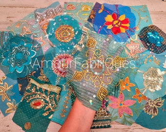 May include: Assortment of teal, blue and pink fabric scraps with gold and silver embroidery and sequins. The fabric scraps are arranged on a light wood surface. The text "Amour Fabriques" is visible in the centre of the image.