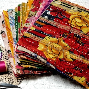 May include: A stack of colorful fabric squares with floral patterns, some with stripes and embroidery. The fabric squares are arranged in a fan shape, with the top square showing a yellow and red floral design.