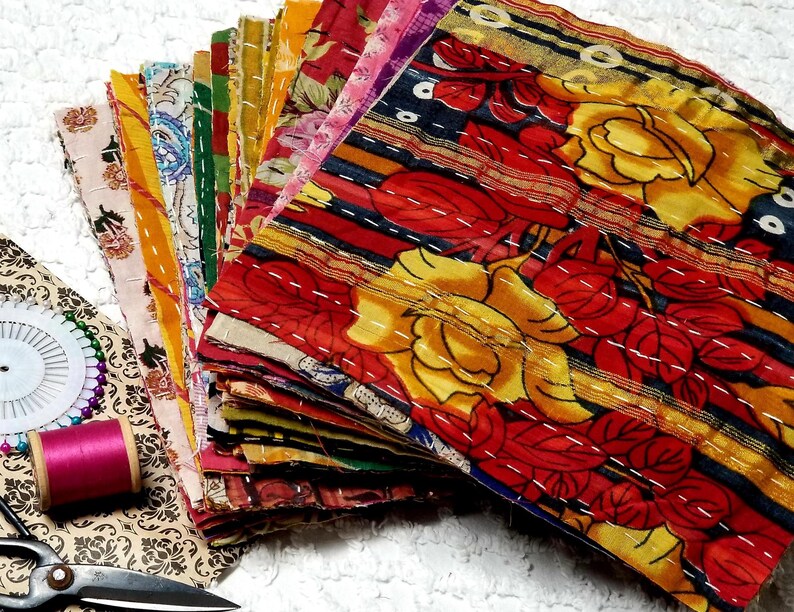 May include: A stack of colorful fabric squares with floral patterns, some with stripes and embroidery. The fabric squares are arranged in a fan shape, with the top square showing a yellow and red floral design.