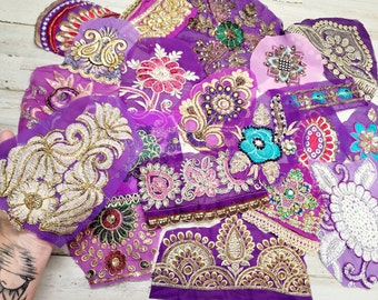 May include: A selection of purple fabric patches with detailed embroidery in gold, silver, and other colours. The patches showcase floral and paisley patterns, adorned with beads and sequins. The fabrics are arranged in a layered composition.