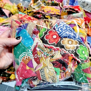 May include: A clear plastic bag filled with colorful fabric scraps. The fabric scraps are a mix of different patterns and textures, including floral prints, paisley designs, and geometric shapes. The bag is labeled "Amour fabriques".