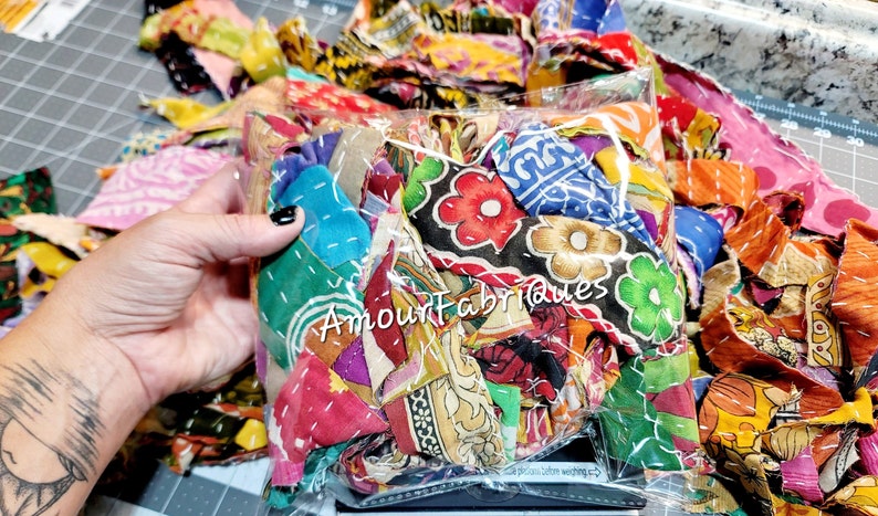May include: A clear plastic bag filled with colorful fabric scraps. The fabric scraps are a mix of different patterns and textures, including floral prints, paisley designs, and geometric shapes. The bag is labeled "Amour fabriques".