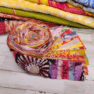 May include: A roll of colorful fabric scraps, tied together with a white string. The fabric is a mix of patterns and colors, including pink, yellow, blue, and green. The fabric is labeled "Amour Fabriques".