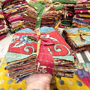 May include: A stack of colorful fabric squares tied with a ribbon. The fabric squares are made of kantha, a type of Indian hand-stitched quilting.