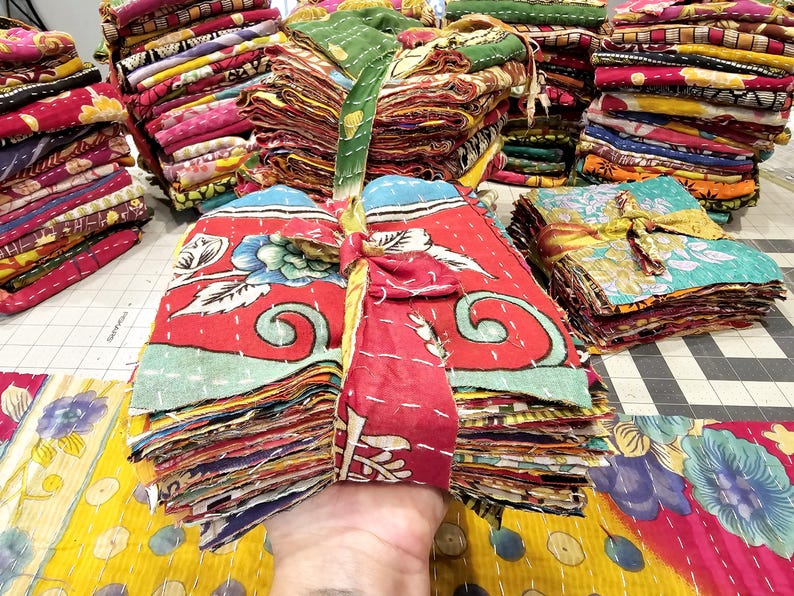 May include: A stack of colorful fabric squares tied with a ribbon. The fabric squares are made of kantha, a type of Indian hand-stitched quilting.
