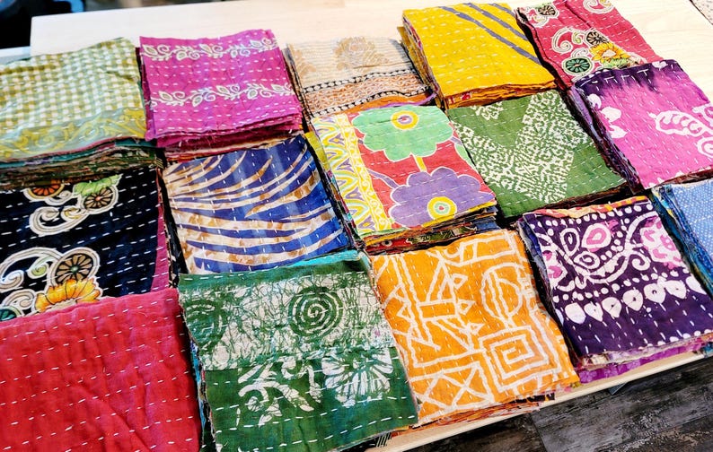 May include: A collection of colorful fabric squares with various patterns, including floral, geometric, and paisley designs. The squares are stacked and arranged in a grid pattern, creating a visually appealing and textured display.