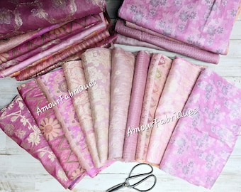 May include: A collection of pink and purple fabric scraps with floral patterns. The fabric is arranged in a fan shape with the text "Amour Fabriques" printed on several of the pieces.