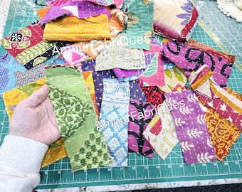 May include: A collection of colorful fabric scraps, some with floral patterns, arranged on a green cutting mat. The fabric scraps are various sizes and shapes, and some have been stitched together. The text "Amour Fabriques" is visible on two of the scraps.