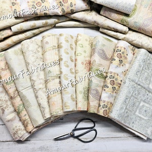 May include: A collection of 14 fabric squares in various shades of beige and green with different floral and paisley patterns. The fabric squares are arranged in a semi-circle with the text "Amour Fabriques" printed on several of the squares. A pair of scissors is in the foreground.