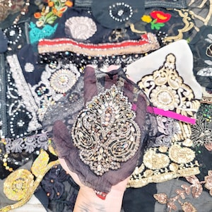May include: An assortment of black fabric pieces with intricate embroidery and embellishments. The designs include floral patterns, sequins, and beadwork in gold, silver, and various colors. Some pieces have a sheer, delicate texture.