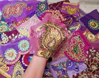 May include: Assortment of purple and pink fabric scraps with intricate gold and jewel-toned embroidery. The fabric scraps feature paisley and floral patterns.