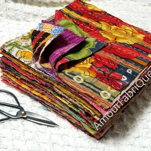 May include: A stack of colorful fabric squares, each with a different pattern, are neatly arranged. The fabric squares are made of a variety of materials, including cotton and silk. The squares are all about 12 inches by 12 inches in size. A pair of black scissors is lying on a white surface in the foreground.