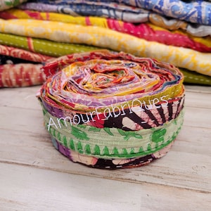 May include: A roll of colorful fabric scraps, tied together with a green fabric strip. The fabric scraps are a mix of floral, paisley, and geometric patterns. The text "Amour_Fabriques" is visible on the fabric.