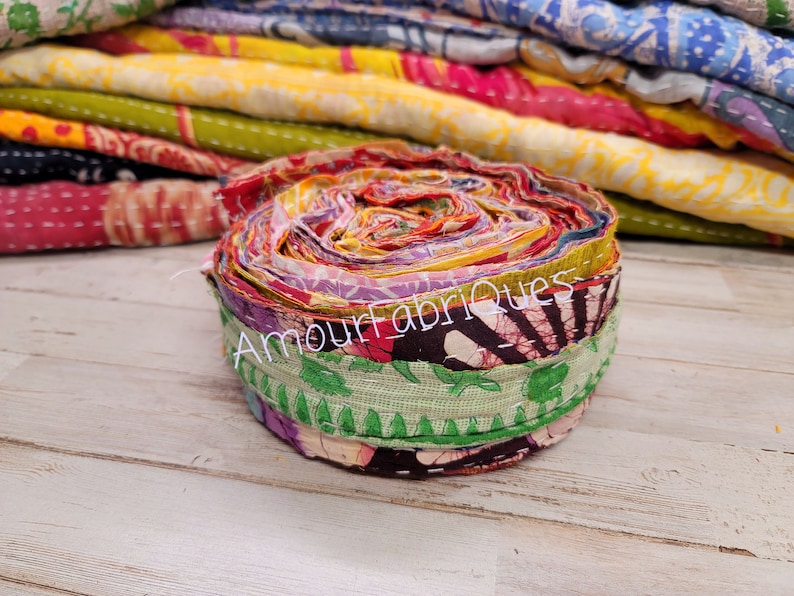 May include: A roll of colorful fabric scraps, tied together with a green fabric strip. The fabric scraps are a mix of floral, paisley, and geometric patterns. The text "Amour_Fabriques" is visible on the fabric.