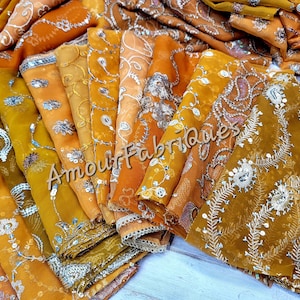 Puede incluir: Una pila de cuadrados de tela de color amarillo dorado con bordados y lentejuelas plateadas. La tela es fina y delicada, y el bordado es intrincado. La tela está etiquetada con "Amour Fabriques".