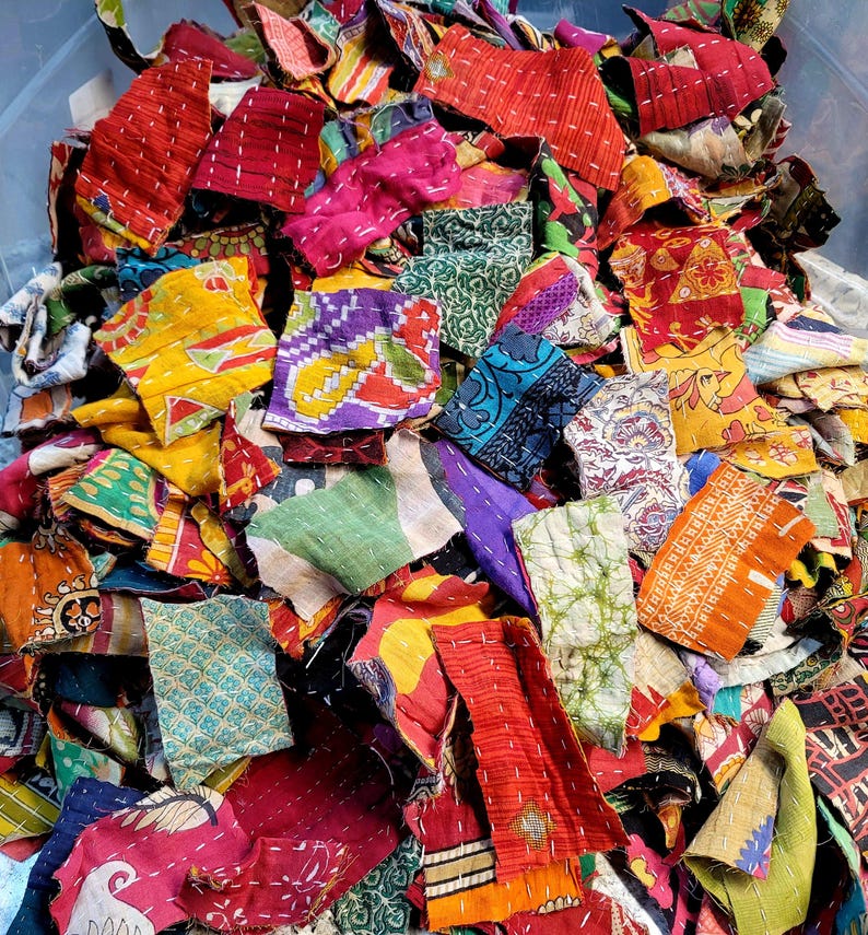 May include: A pile of colorful fabric scraps, perfect for quilting or other craft projects. The scraps are made of various fabrics, including cotton, silk, and linen. They are all different sizes and shapes, and some have been stitched together.