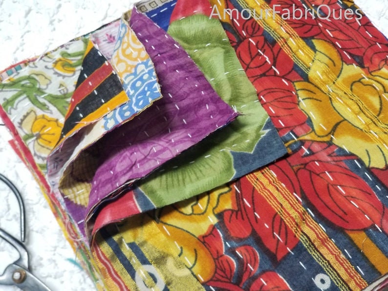 May include: A stack of colorful fabric squares with floral patterns, stitched together with white thread. The fabric is a mix of red, yellow, green, blue, and purple.