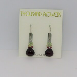 May include: A pair of dangle earrings with a dark purple gemstone, green and pink beads, and silver hooks. The earrings are displayed on a white card with the text "THOUSAND FLOWERS PRECIOUS STONES".