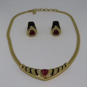 May include: A gold-toned necklace and matching earrings set. The necklace and earrings feature black enamel accents and red, triangular-shaped stones. The earrings and necklace have a gold chain.
