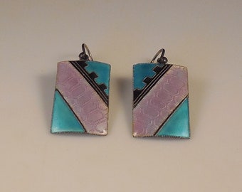 May include: A pair of silver earrings with a geometric design. The earrings are rectangular and feature a turquoise, pink, and black enamel pattern.