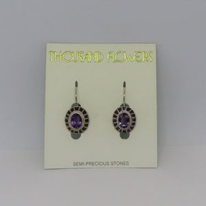 Può includere: Un paio di orecchini d'argento con pietre di ametista viola incastonate in una cornice d'argento. Gli orecchini sono su una carta bianca con il testo "THOUSAND FLOWERS" e "SEMI-PRECIOUS STONES".