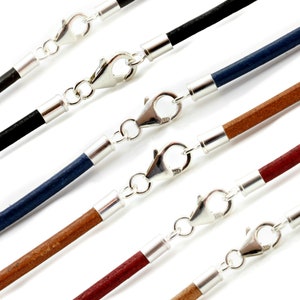 May include: Close-up of several leather cord necklaces in various colours, including black, blue, brown, and red. Each necklace features a silver-coloured clasp and end caps, creating a simple yet elegant design. The cords are approximately 2mm in diameter.