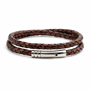 May include: A brown leather bracelet with a braided design. The bracelet wraps around twice and features a silver-colored magnetic clasp. The leather has a textured appearance.