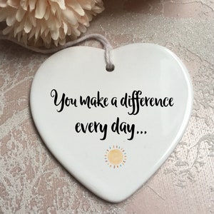 May include: White ceramic heart-shaped ornament with the text "You make a difference every day..." and a small yellow sun with orange rays.