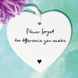 May include: White ceramic heart-shaped ornament with the text "Never forget the difference you make" in black cursive writing and a small black heart at the bottom.
