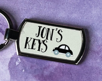 May include: A silver keychain with a white rectangular tag that says "JON'S KEYS" in black text with a small black car graphic.