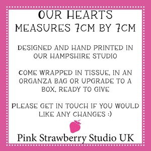 May include: A white square sign with a pink border and white dots, featuring black text: OUR HEARTS MEASURES 7CM BY 7CM, DESIGNED AND HAND PRINTED IN OUR HAMPSHIRE STUDIO, COME WRAPPED IN TISSUE, IN AN ORGANZA BAG OR UPGRADE TO A BOX, READY TO GIVE, PLEASE GET IN TOUCH IF YOU WOULD LIKE ANY CHANGES :), a small pink strawberry icon, and Pink Strawberry Studio UK.