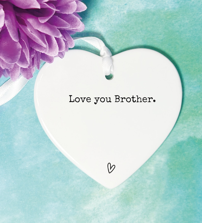 May include: White ceramic heart-shaped ornament with the text "Love you Brother." in black lettering. A small heart is drawn at the bottom of the ornament.