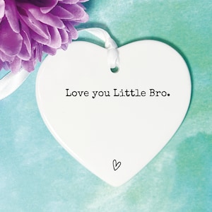May include: White ceramic heart-shaped ornament with the text "Love you Little Bro." in black lettering. A small heart is drawn at the bottom of the ornament.