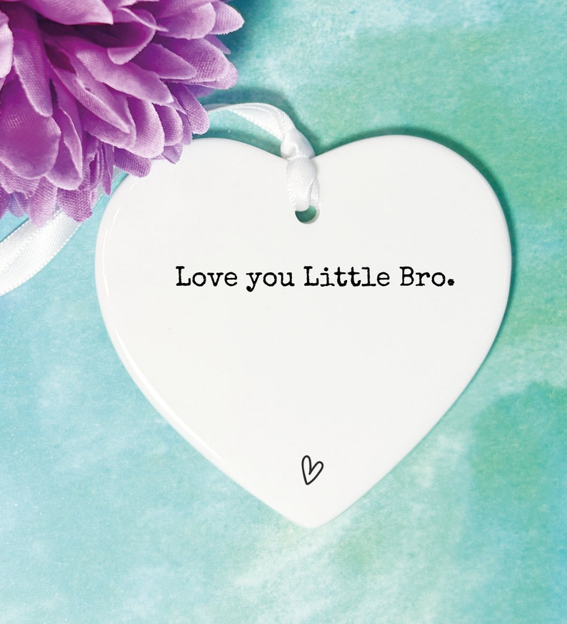 May include: White ceramic heart-shaped ornament with the text "Love you Little Bro." in black lettering. A small heart is drawn at the bottom of the ornament.