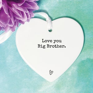 May include: White ceramic heart-shaped ornament with a white ribbon. The ornament has the text "Love you Big Brother." printed in black.